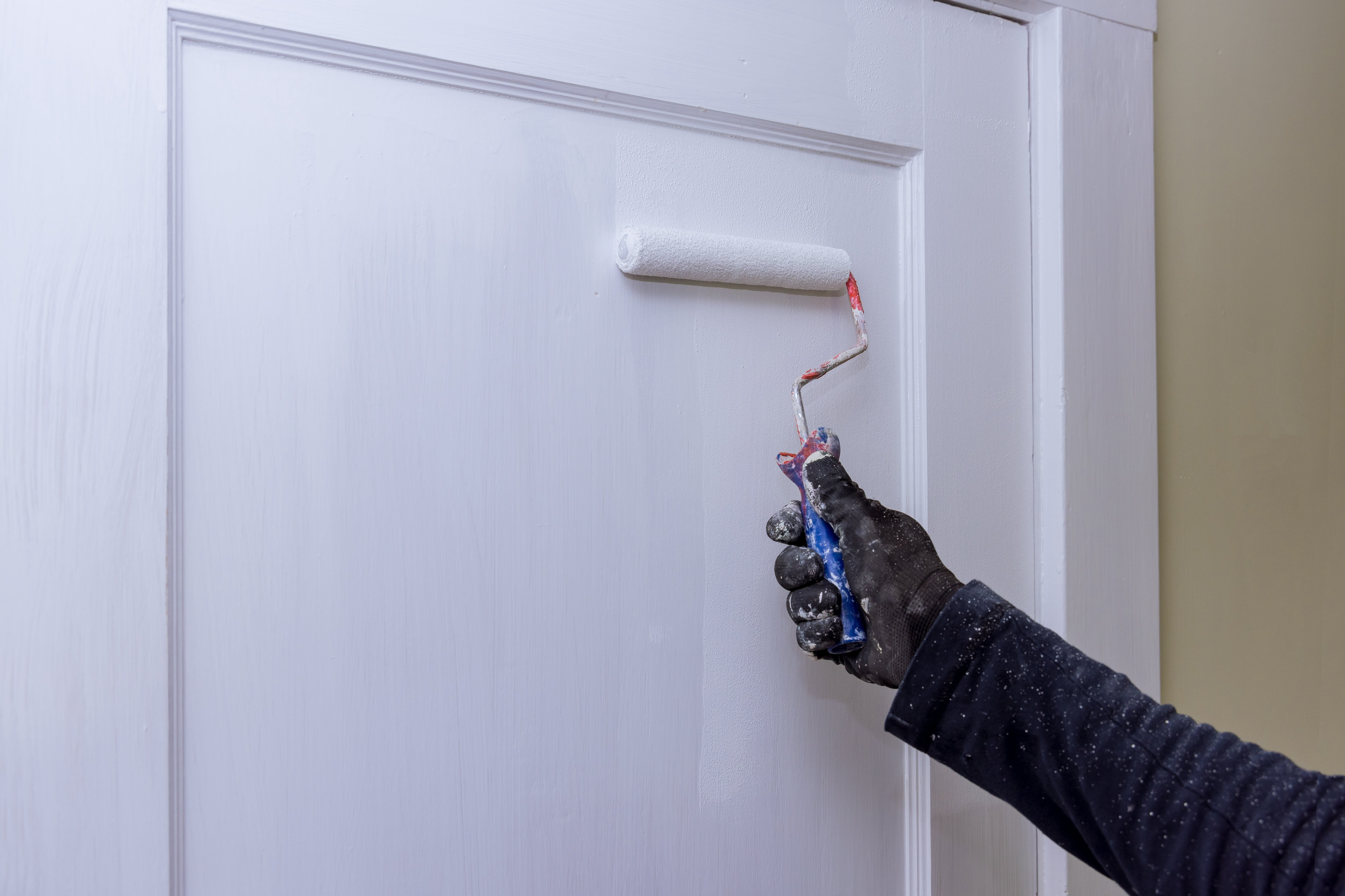 Gloved hand painting a flat door white with a mini roller